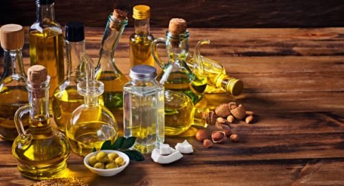 Assorted healthy vegetable oil bottle collection on wooden table in a old fashioned kitchen with low key illumination: Olive oil, hazelnut oil, almond oil, coconut oil and sesame oil